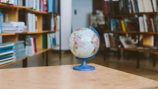 A globe in a quiet library setting, surrounded by shelves filled with books, represents education and exploration.
